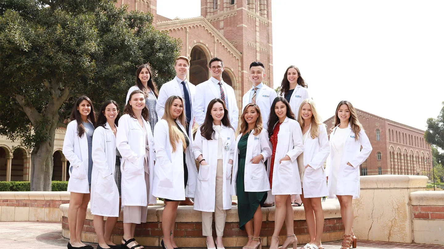 A group of nursing students wearing white coats and standing in front of the Royce Hall towers.