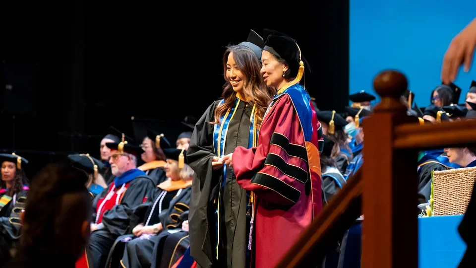A student on stage with Dean Lin Zhan at commencement