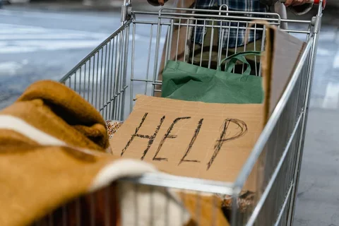 A photograph of a homeless person's shopping cart with a sign saying Help