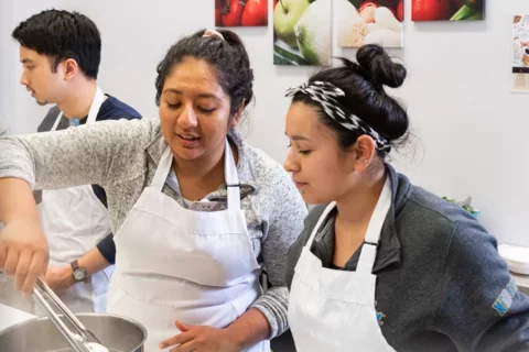 Two SON students in a kitchen wearing aprons and cooking