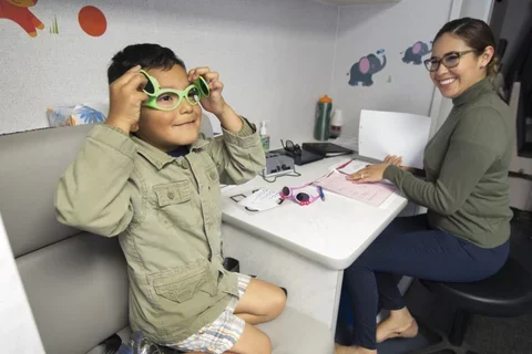 A child sitting with a provider and trying on glasses