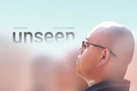 A bald young man appears in-focus, amidst hazy ﬁgures surrounding him. He wears glasses while looking up to the endless bright sky above him, his expression pensive. As the sky meets the young man’s head in the middle of the poster, the ﬁlm’s title appears: unseen.