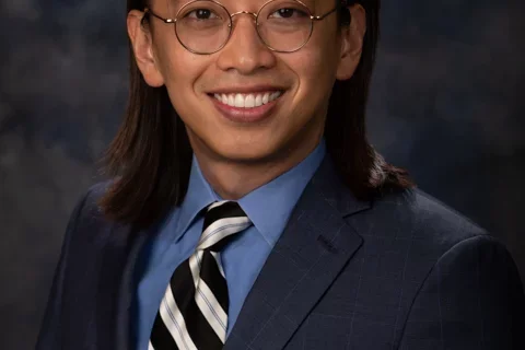 Man with long hair and glasses wearing a suit