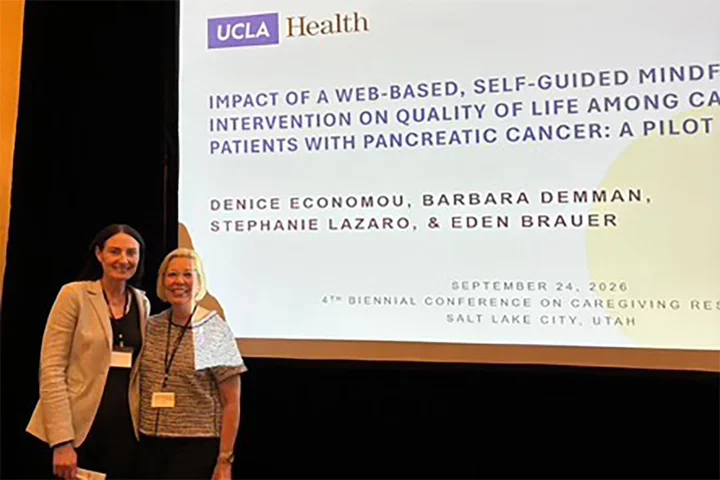 Eden Brauer and Denice Economou standing in front of a display screen at a recent conference presentation.