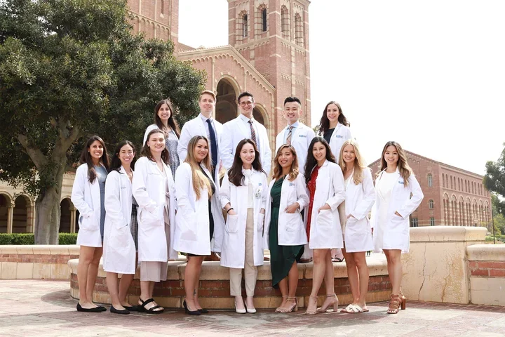 A group of nursing students wearing white coats and standing in front of the Royce Hall towers.