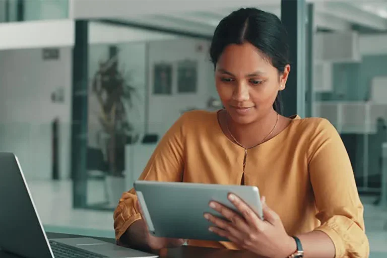 A woman sitting at a desk looking at a tablet