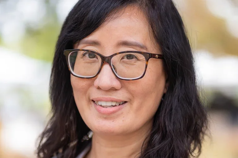 Dr. Suwen Pan wearing black shirt, white lab coat, and glasses.