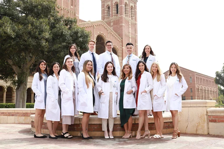 A group of nursing students wearing white coats and standing in front of the Royce Hall towers.
