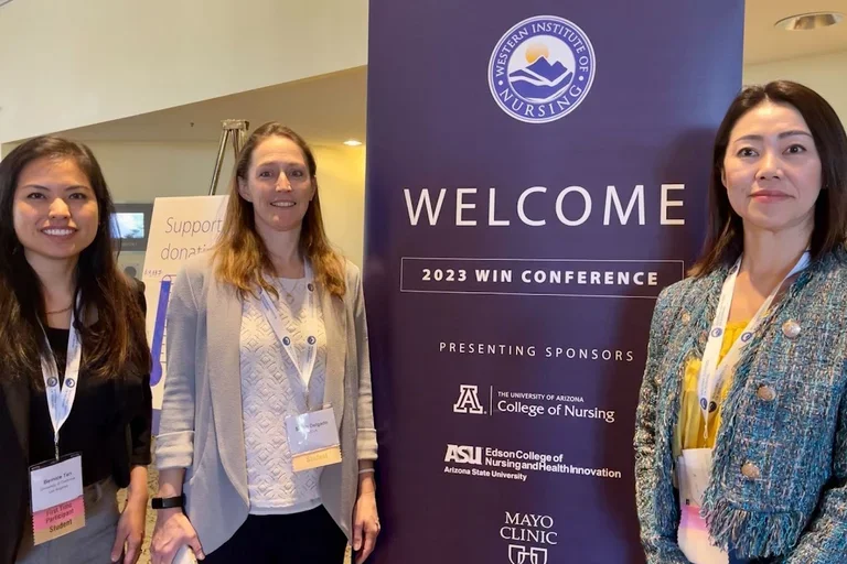 Three students standing at the WIN Conference welcome sign