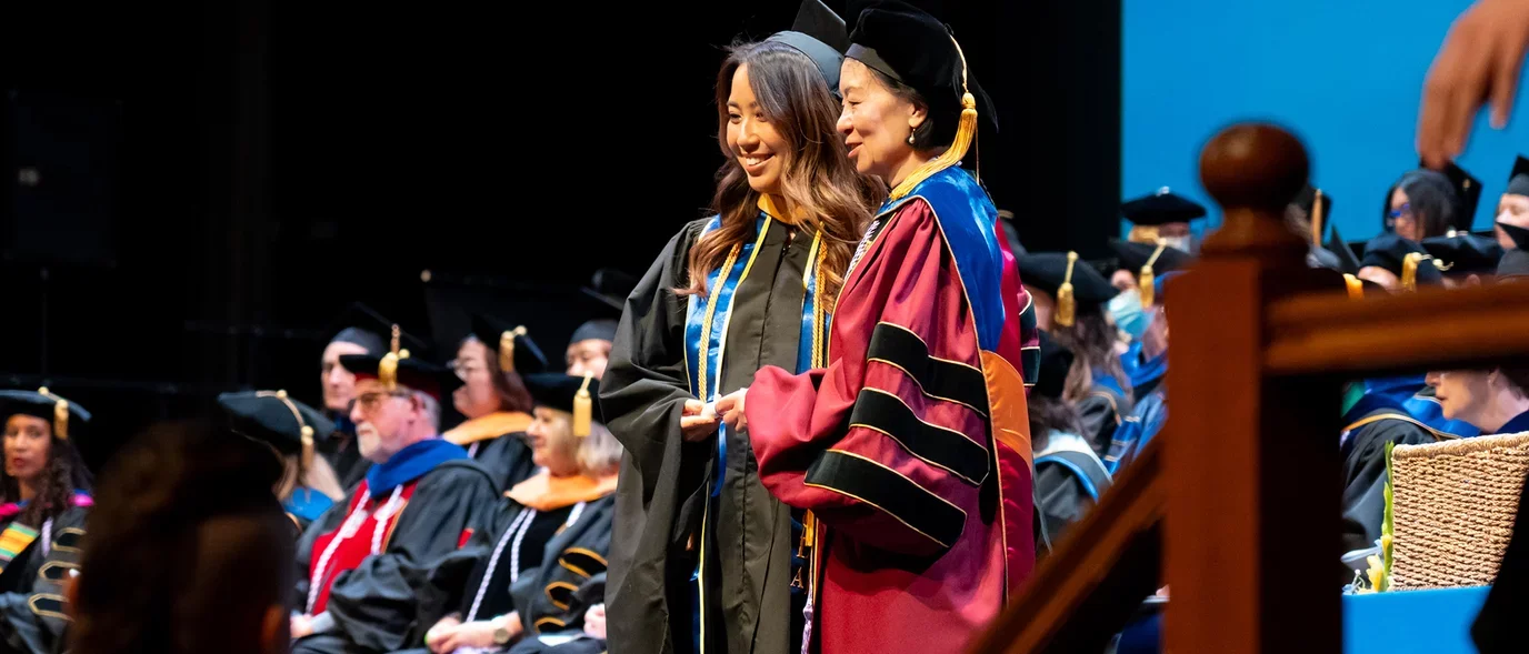 A student on stage with Dean Lin Zhan at commencement