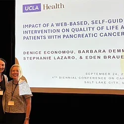 Eden Brauer and Denice Economou standing in front of a display screen at a recent conference presentation.