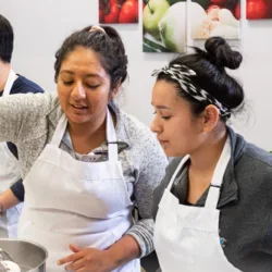 Two SON students in a kitchen wearing aprons and cooking