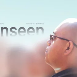 A bald young man appears in-focus, amidst hazy ﬁgures surrounding him. He wears glasses while looking up to the endless bright sky above him, his expression pensive. As the sky meets the young man’s head in the middle of the poster, the ﬁlm’s title appears: unseen.